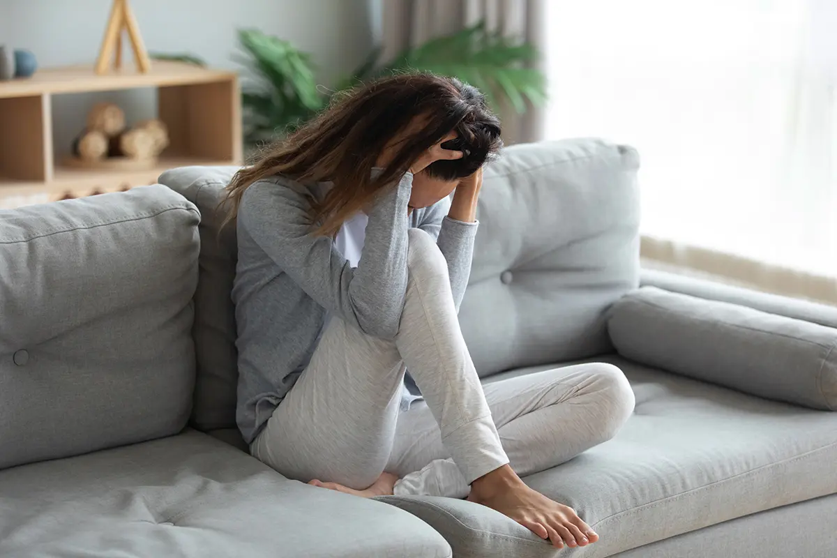 a stressed woman sitting on a sofa with her head in her hands