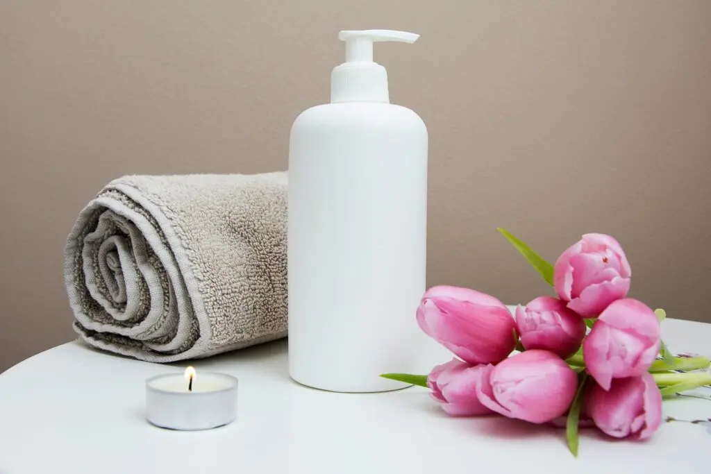 Towel, shampoo, candle and flowers on counter.