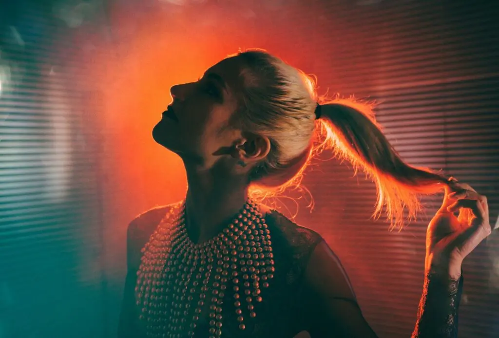 Woman holding her ponytail to the right with a red smokey background.