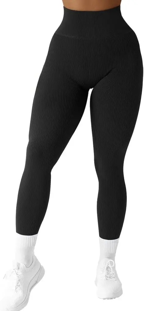 A woman stands in white tennis shoes and tall white socks while wearing ribbed black leggings with a high waist band.