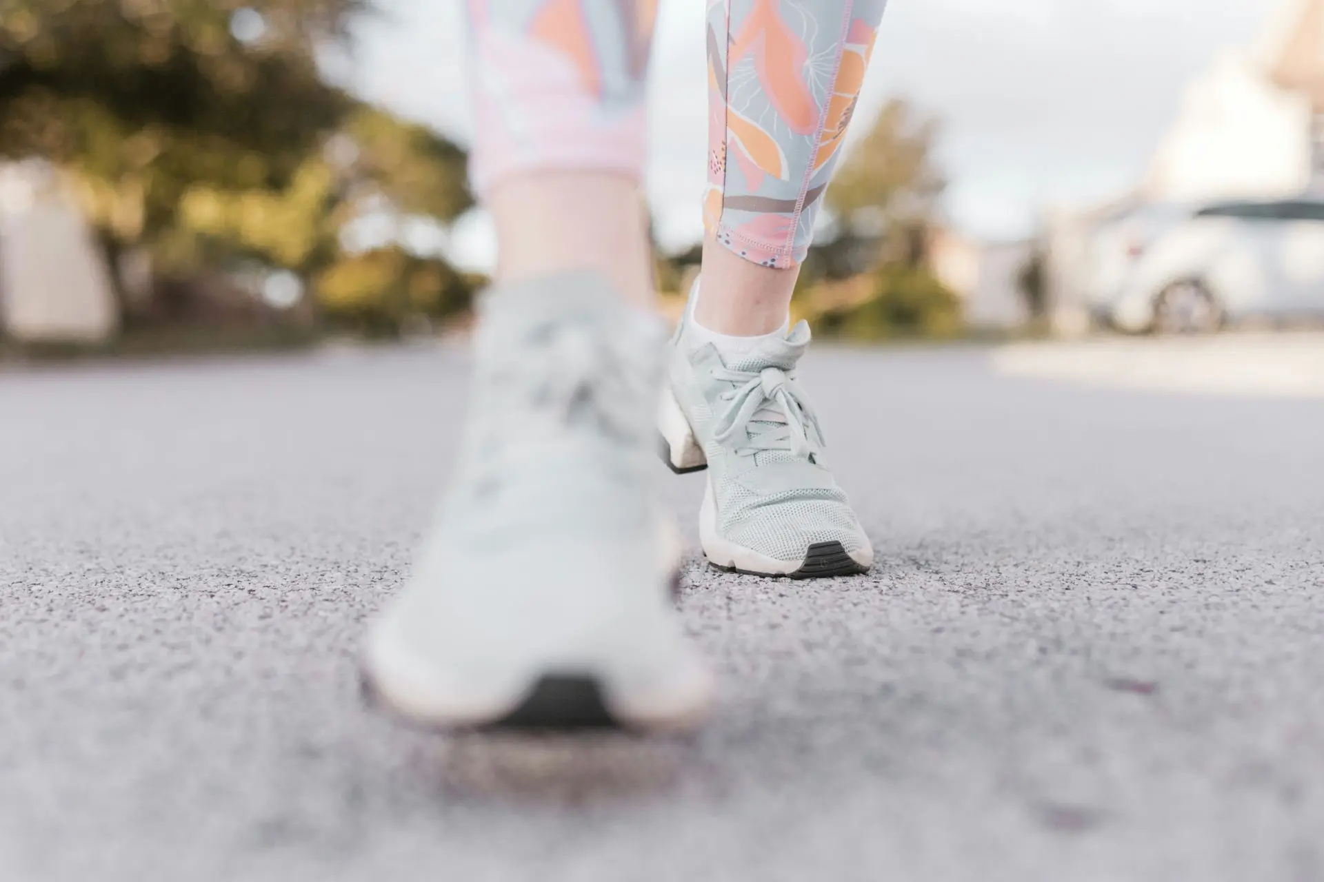 A person's legs and feet in athletic shoes, walking outdoors on a paved path.