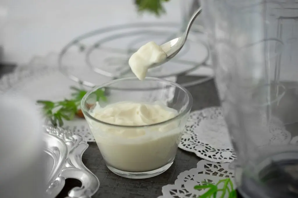 Someone taking a spoonful of white yogurt on a table covered in doilies and dishware.