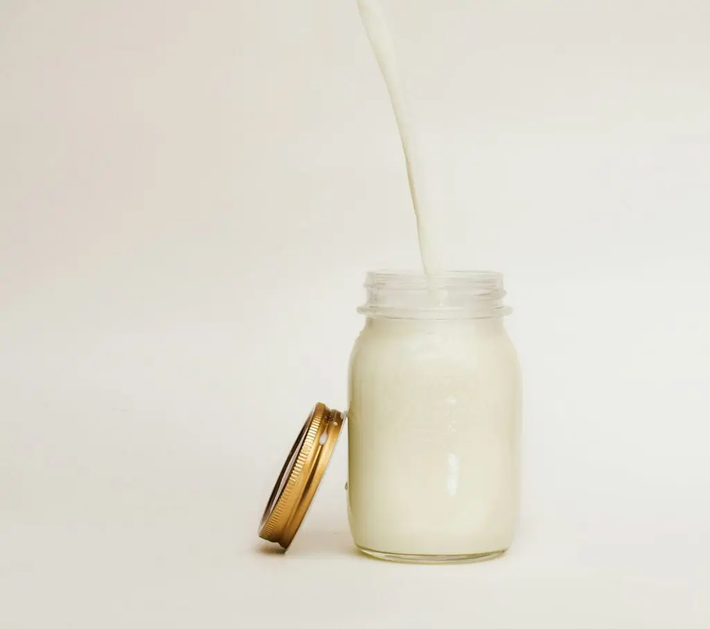 Milk pouring into a mason jar from high above it against a white background.