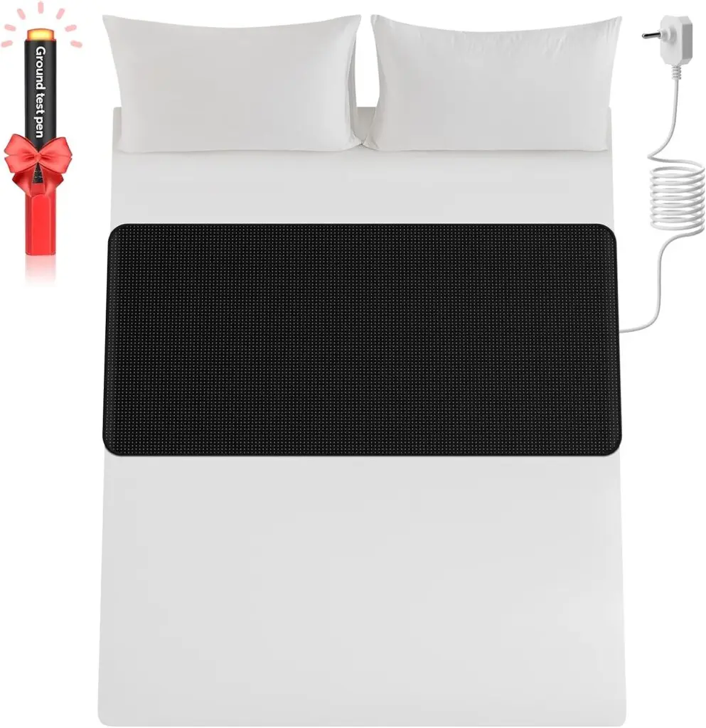 A black grounding mat with a white electrical cord stretches across a queen bed with white sheets, two white pillows and no comforter. The background is white and there's a free black ground test pen wrapped in a red bow in the top left corner.