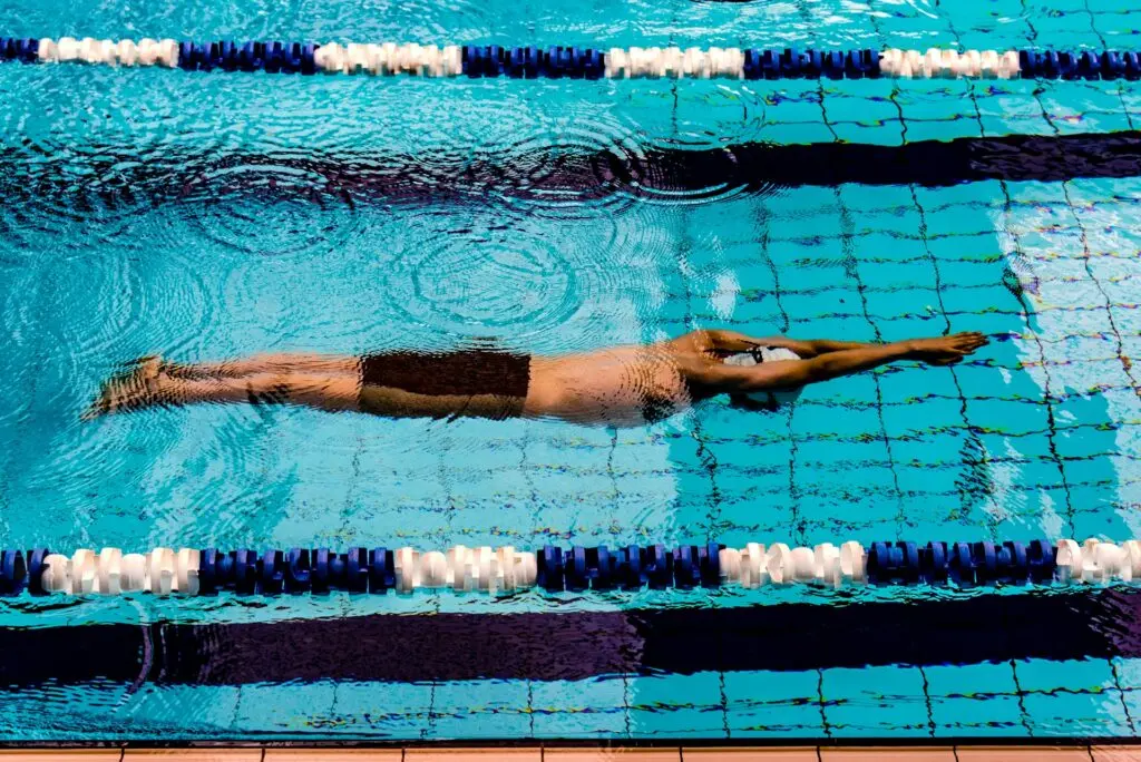 A swimmer keeps their arms pointed out and above their head after flip kicking off the wall of their lane. They are completely underwater. Ripples cover the surface above them from the splash of their flip kick.