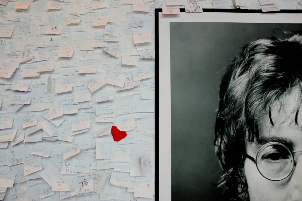 A large photo of John Lennon only shows his right eye and his hair. The other half of the frame includes Post-It notes and a red heart, since people are leaving their names next to the John Lennon photo in tribute of him.