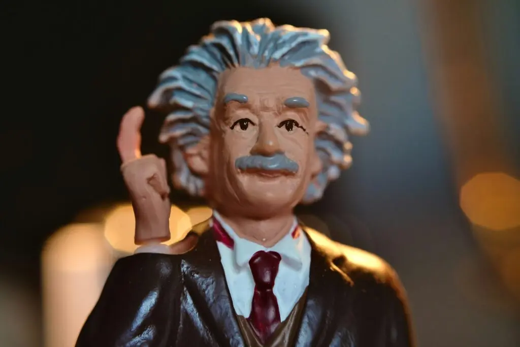 A toy figurine that's slightly aged and resembles Albert Einstein. He holds up a finger to his temple.