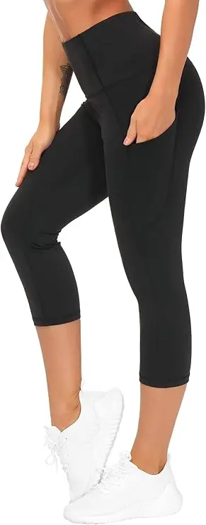A woman stands in white tennis shoes and black stretchy workout leggings. One of her hands is in the pocket of the leggings. The material ends just below the knee and has a high waist.