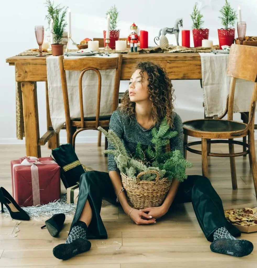 A girl holding a burr basket and sitting on her floor amid Christmas decor