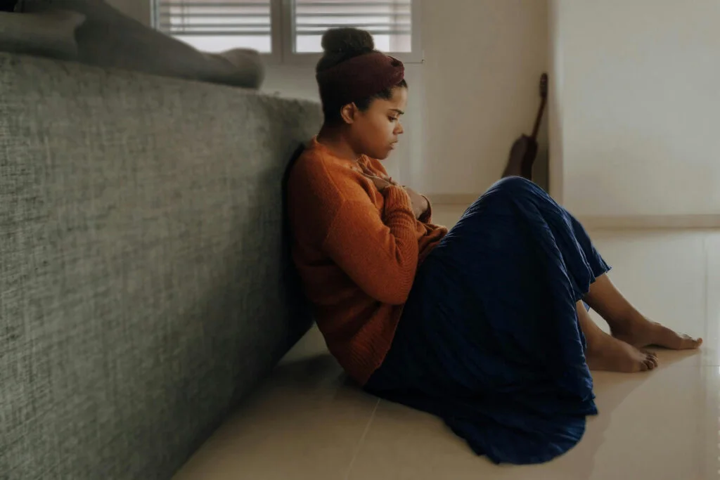 A young woman sitting with her hands on her chest looking anxious