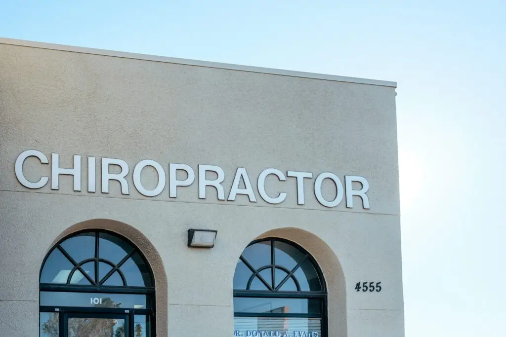 A beige building with two curved windows and one floor has the word "chiropractor" in all caps on the side of the front. A cloudless blue sky is behind the building.
