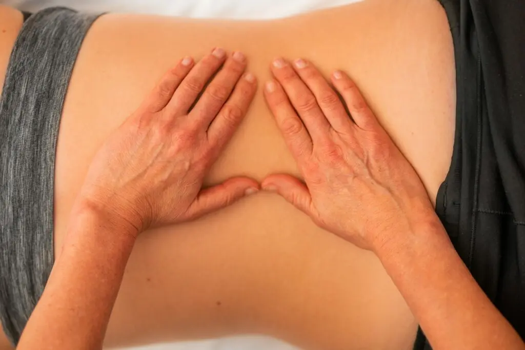 A chiropractor presses both hands into a person's lower spine. The patient is lying face-down on a table.