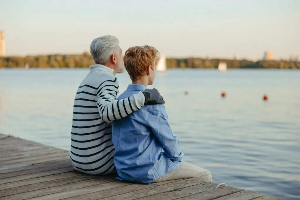 A boy sitting by a lake with his elderly father