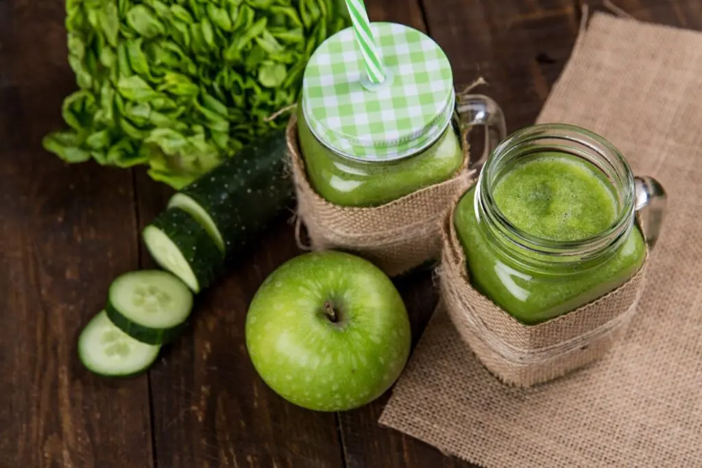A green apple and a cucumber beside two glass jars