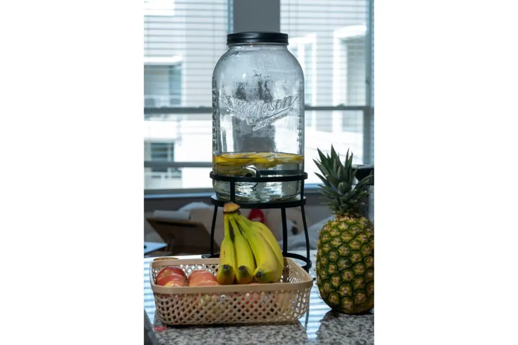 yellow bananas and red apples in a basket next to pineapple fruit and clear glass bottle containing water