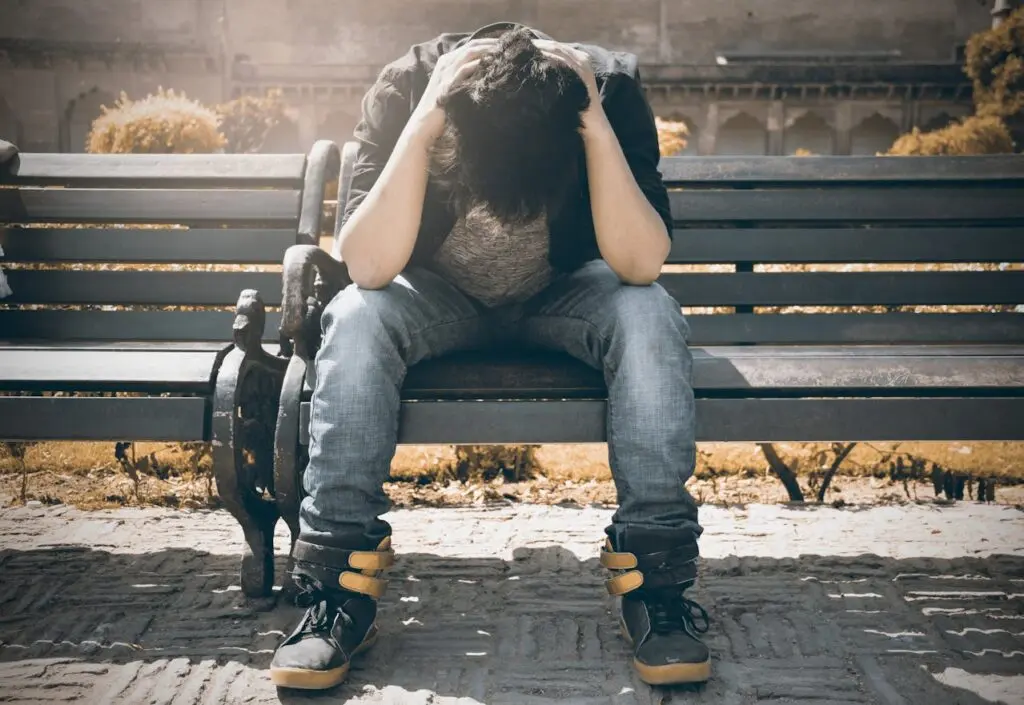 A man sitting on a park bench with his head in his hands