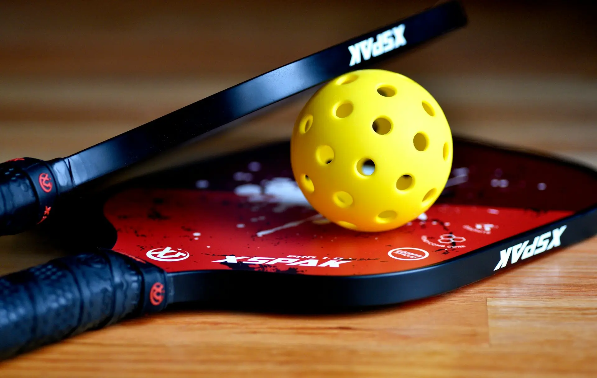 A yellow tennis ball sitting on top of a pickleball racket
