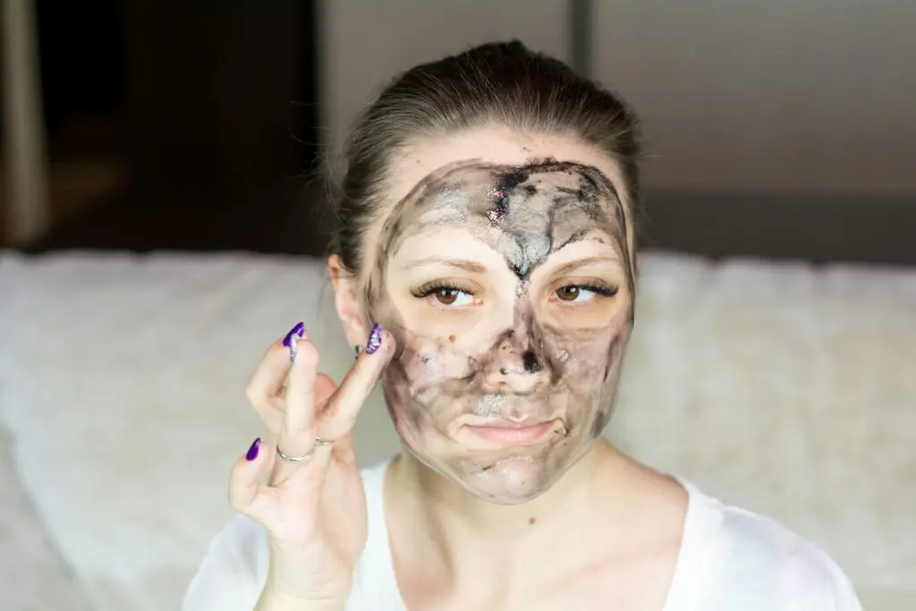A woman applying a skincare mask to her face.