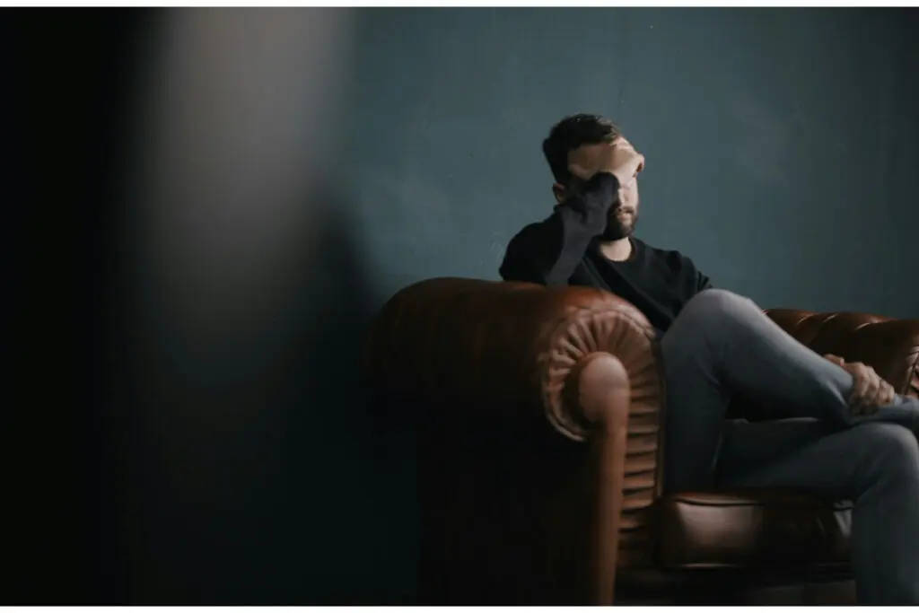 An upset man sitting on a sofa with his head in his hand.