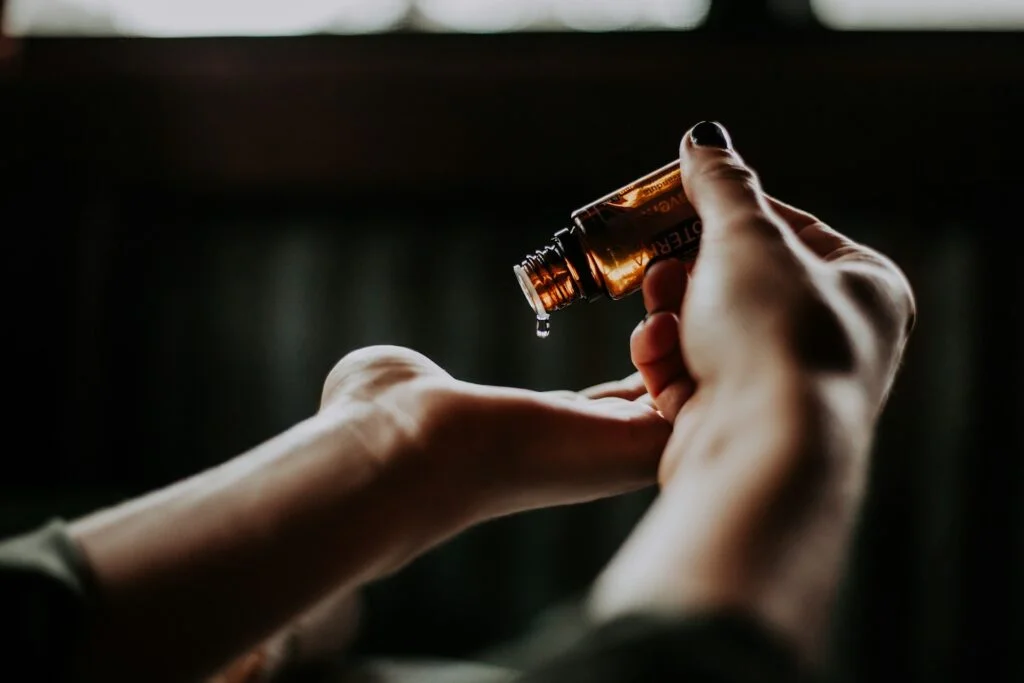 Close-up of hands pouring essential oil from a brown bottle into a palm, capturing a serene and calming atmosphere with a soft, dimly lit background.