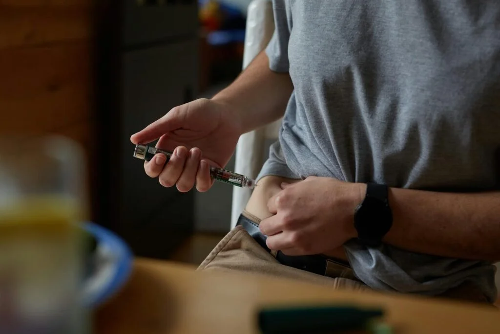 man in gray shirt injecting insulin in stomach