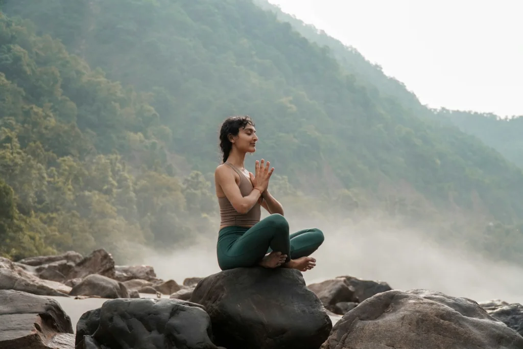 a woman sitting on top of a rock, meditating to manage stress and increase sex drive