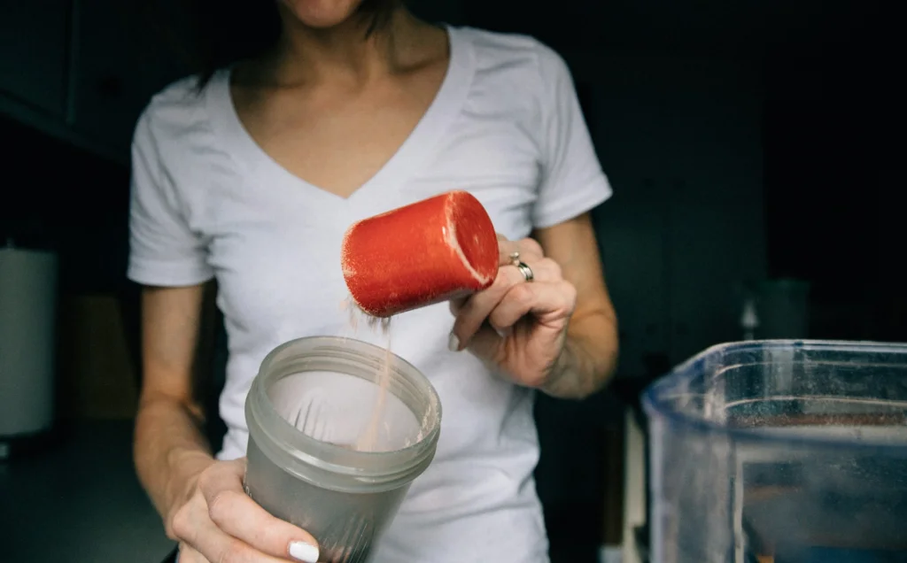 A woman adding a collagen supplement powder into a blender