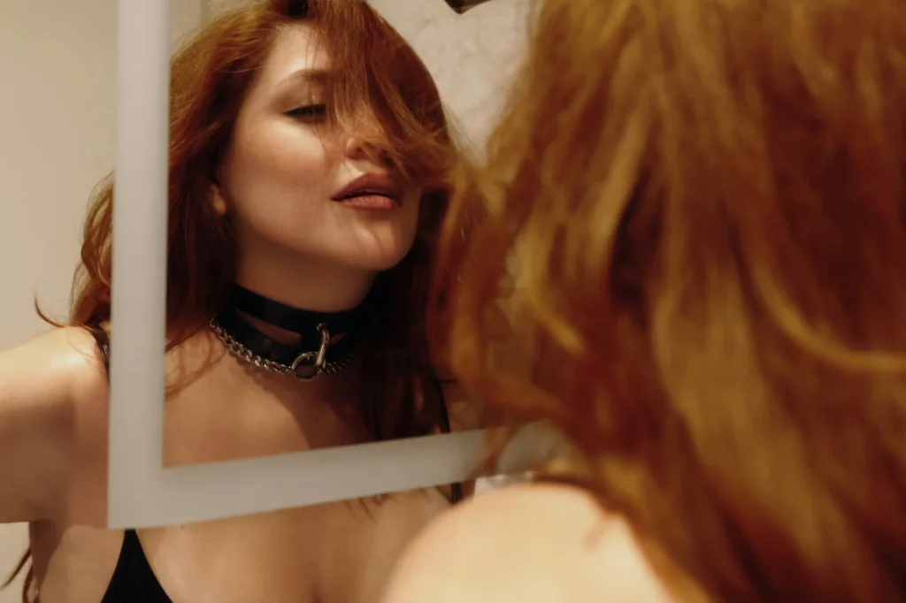 Auburn haired woman with neck chain looking into mirror