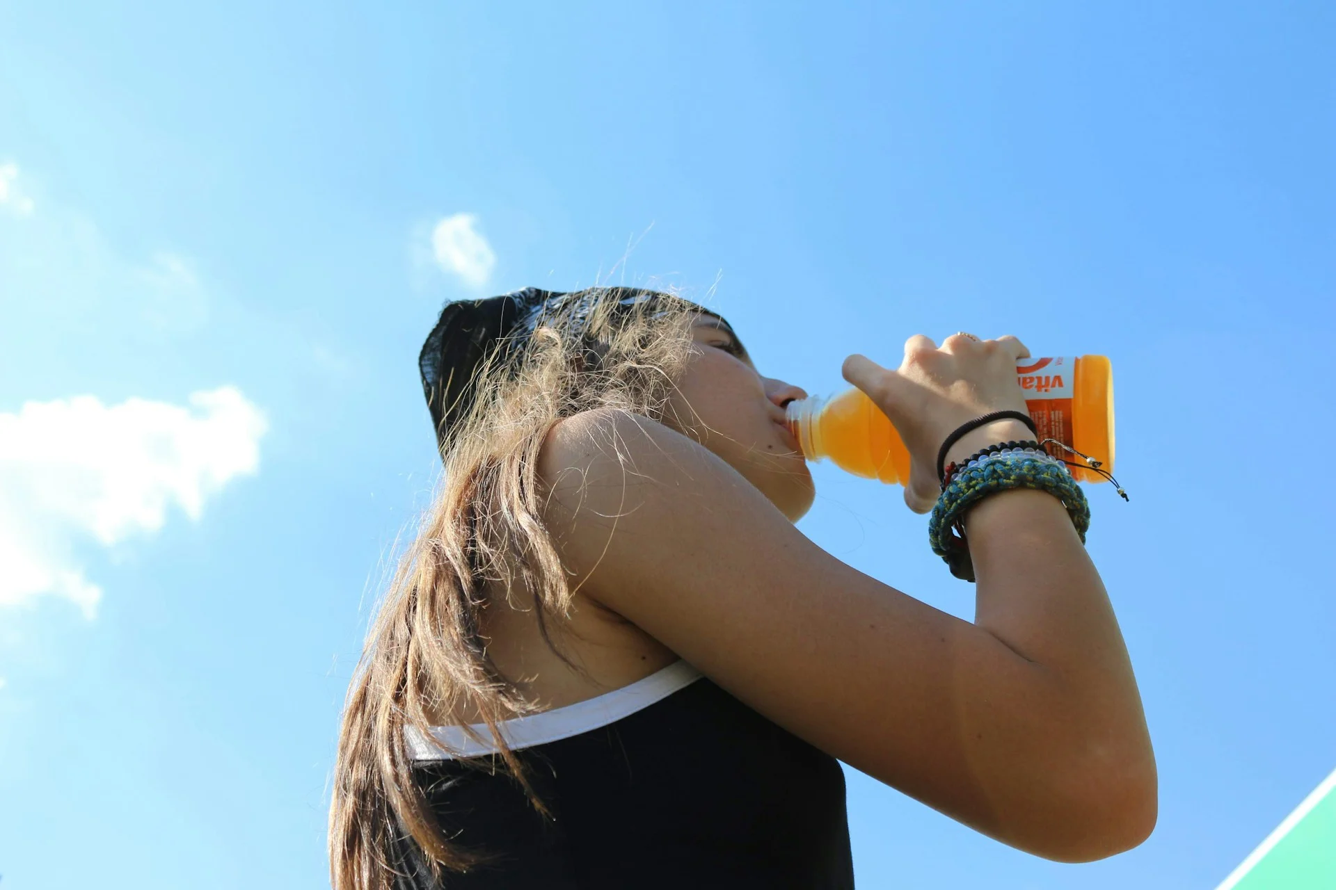 low-angle photography of woman drinking orange on bottle of electrolyte supplement