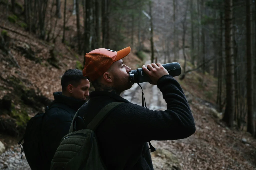 Two men hiking in the woods, one of them is drinking from a water bottle