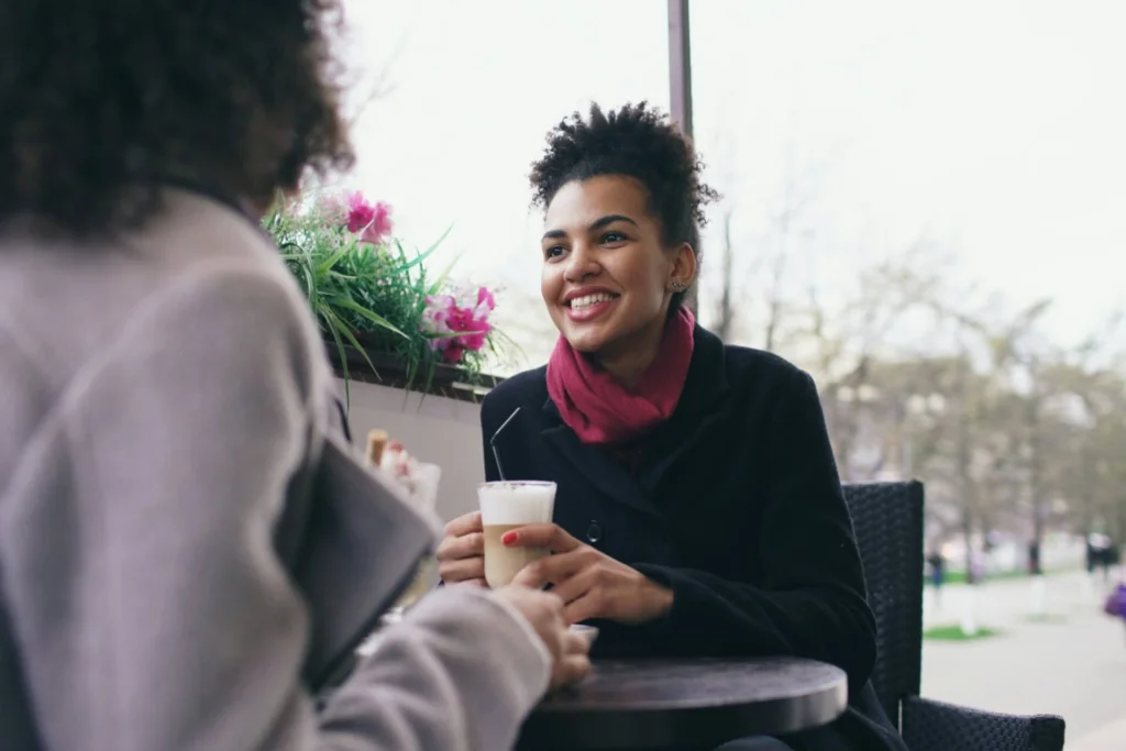 Two people smiling and holding coffee cups while sitting together