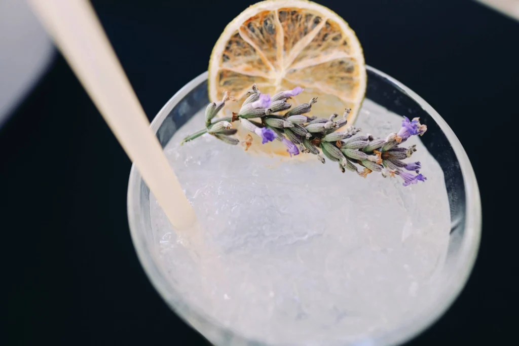 A glass of lavender lemonade over ice, garnished with a lemon slice, a lavender sprig and a straw