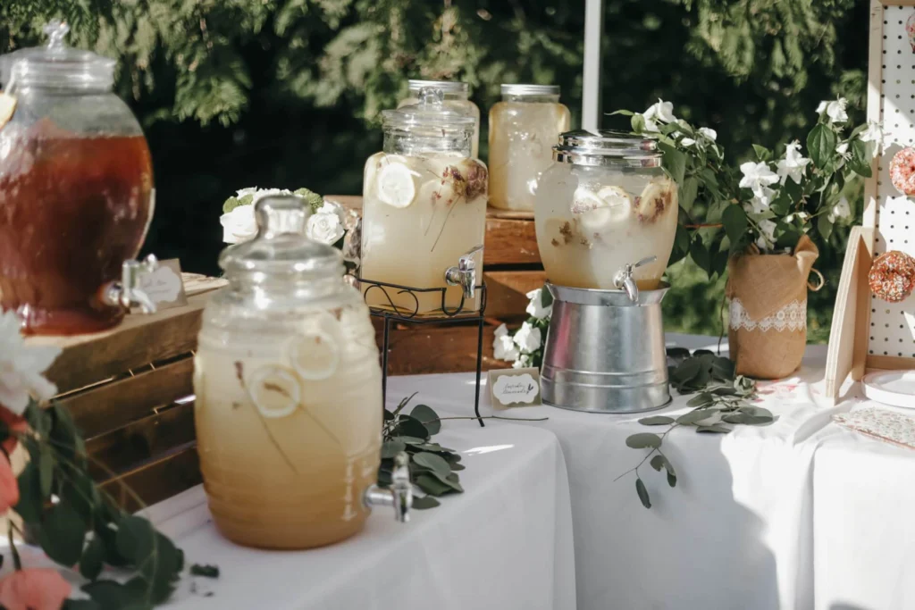 Glass drink dispensers filled with a cloudy lavender lemonade, lemon slices and dried flowers