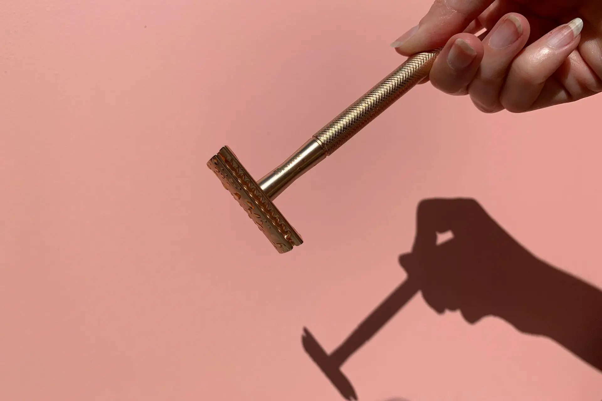 A hand holding one of the best bikini trimmers against a pink backdrop
