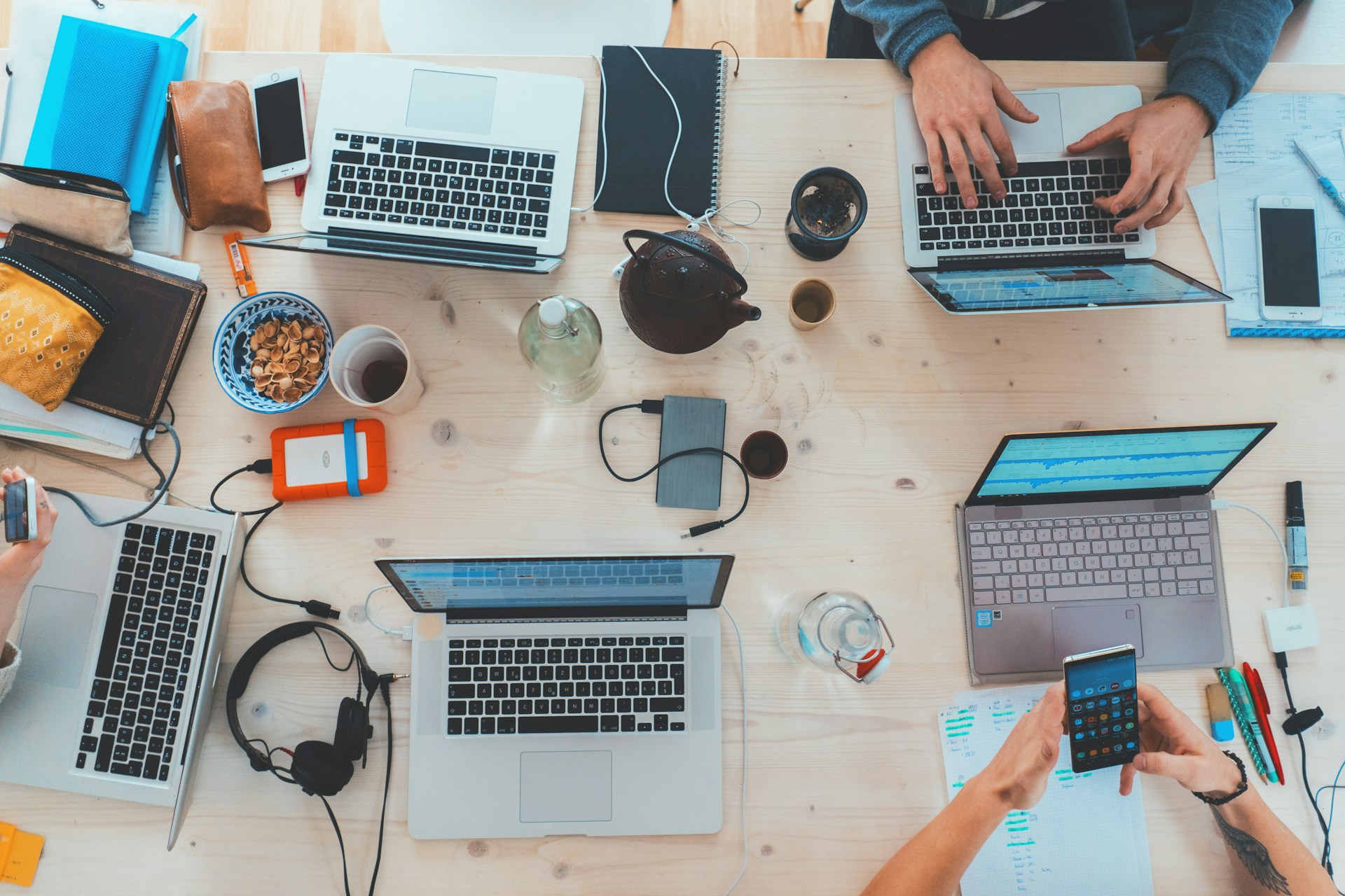 A diverse group of individuals collaborating at a table, each focused on their laptops in a modern workspace.