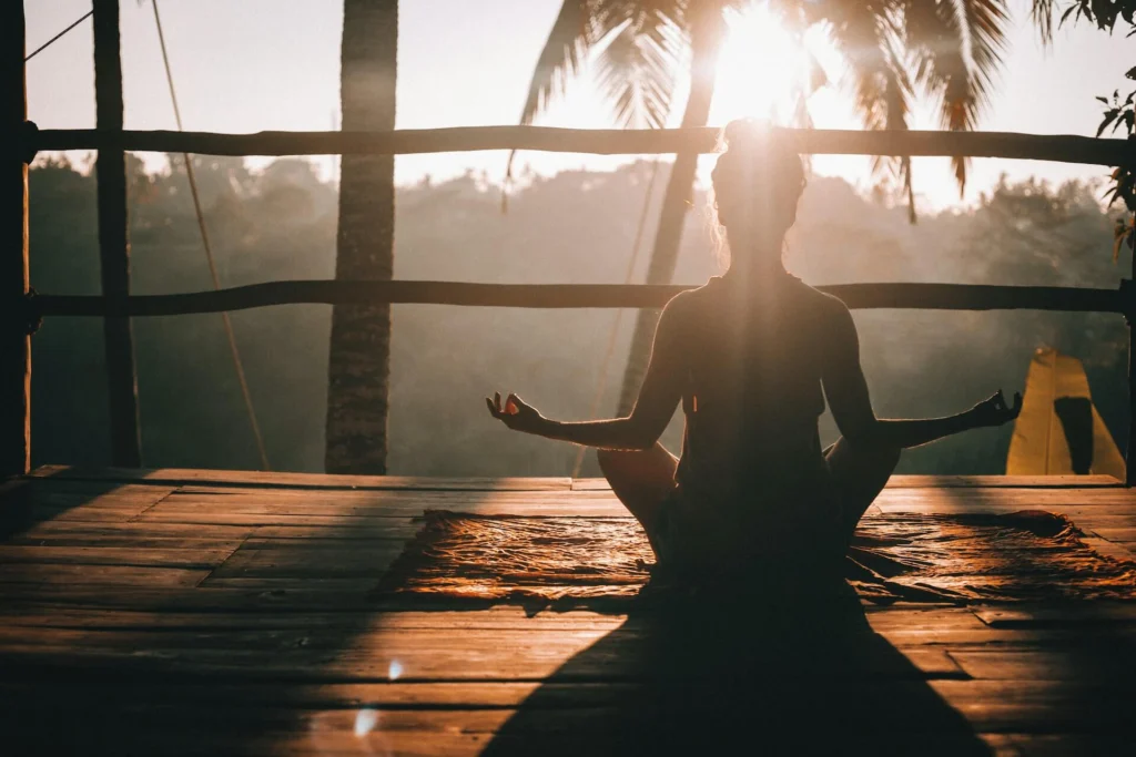 Woman sitting in a calming pose on a wooden dock overlooking the jungle at sunrise
