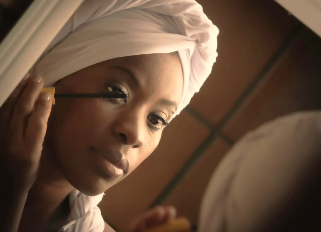 Woman in a white hijab smiling while applying makeup in front of a mirror