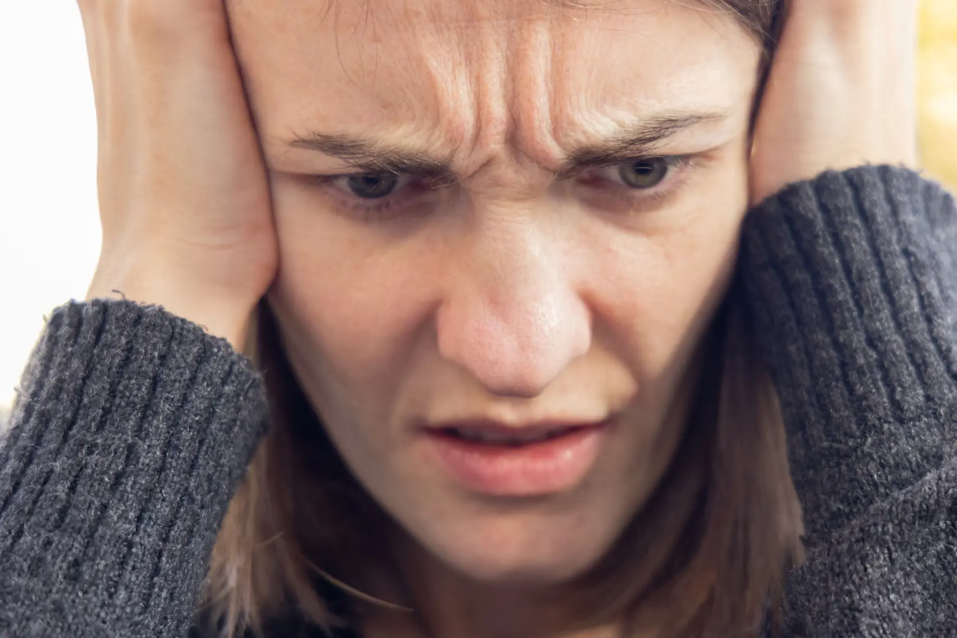 woman in gray holding head and frowning