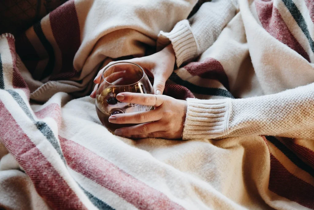 A person wrapped up in a blanket, holding a drink