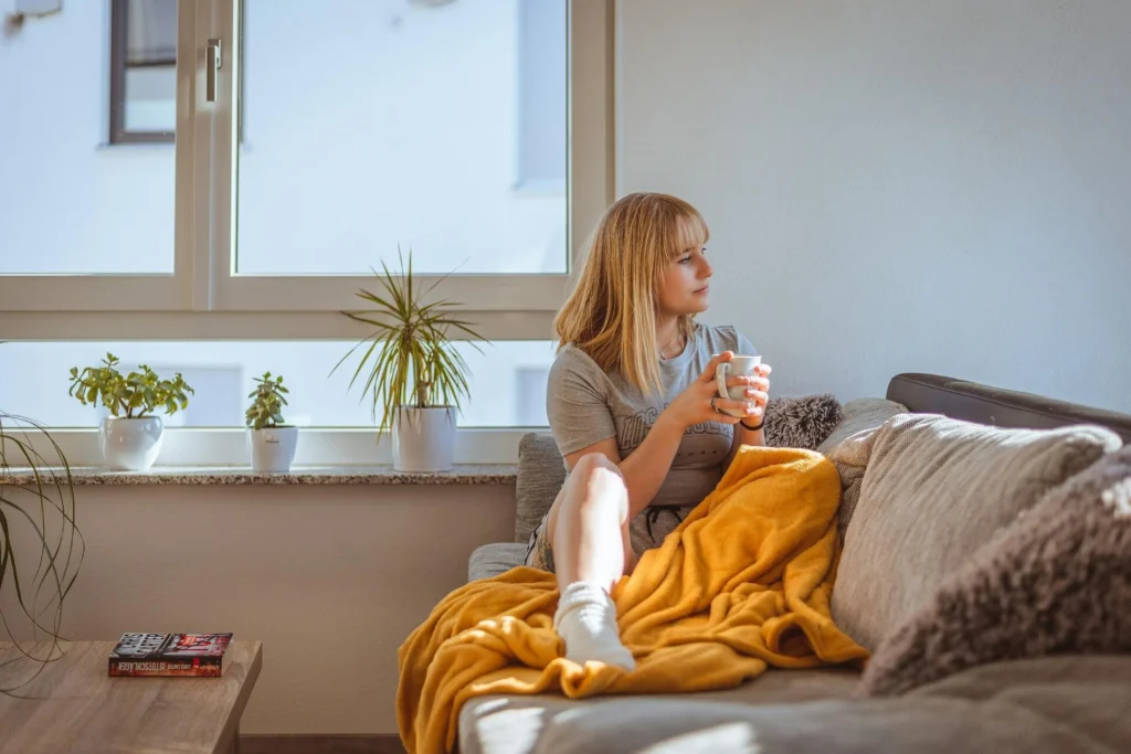 a woman looking at a distance while sitting on a couch and holding a cup