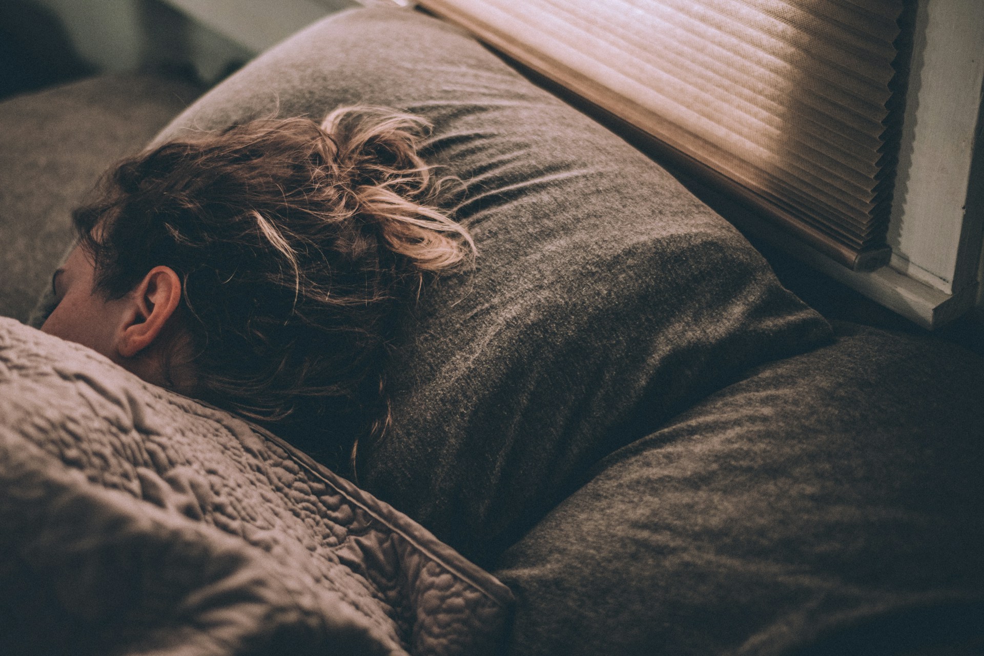 A woman peacefully sleeping in bed, covered with a cozy blanket.