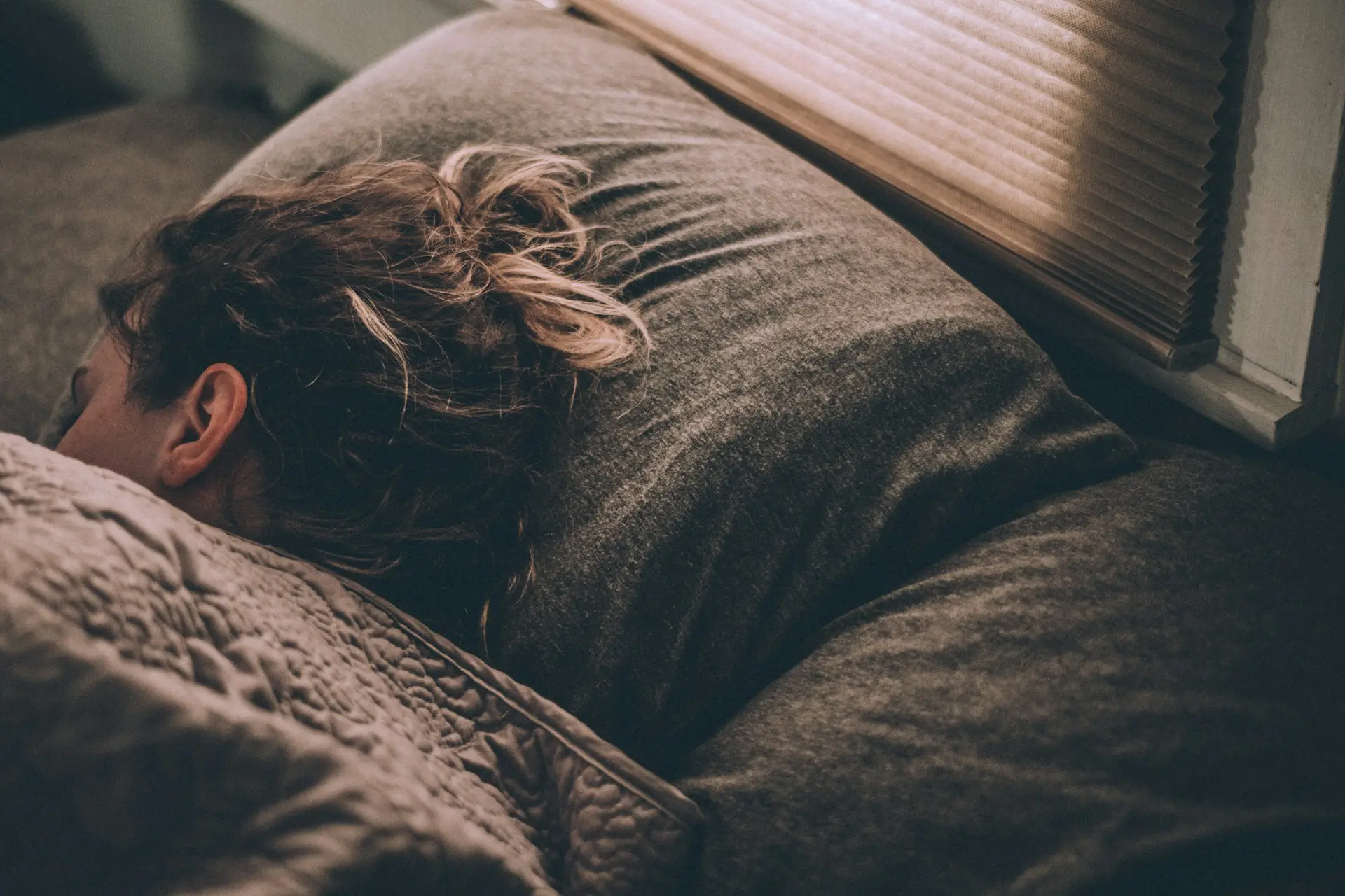 A woman peacefully sleeping in bed, covered with a cozy blanket.
