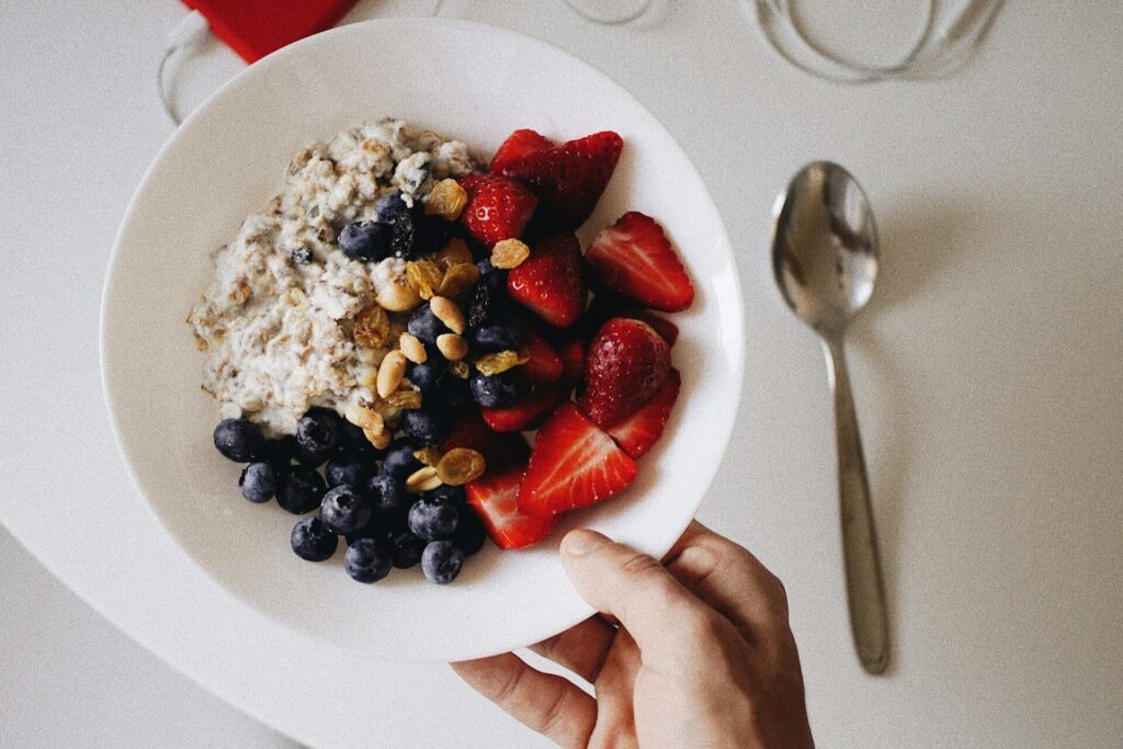 a person holding a bowl of oatmeal topped with nuts and berries