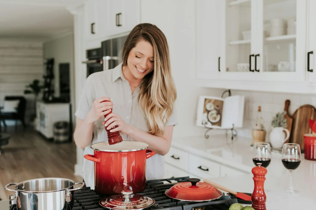 A woman prepares a meal in a kitchen, surrounded by vibrant red pots on the stove and countertops.