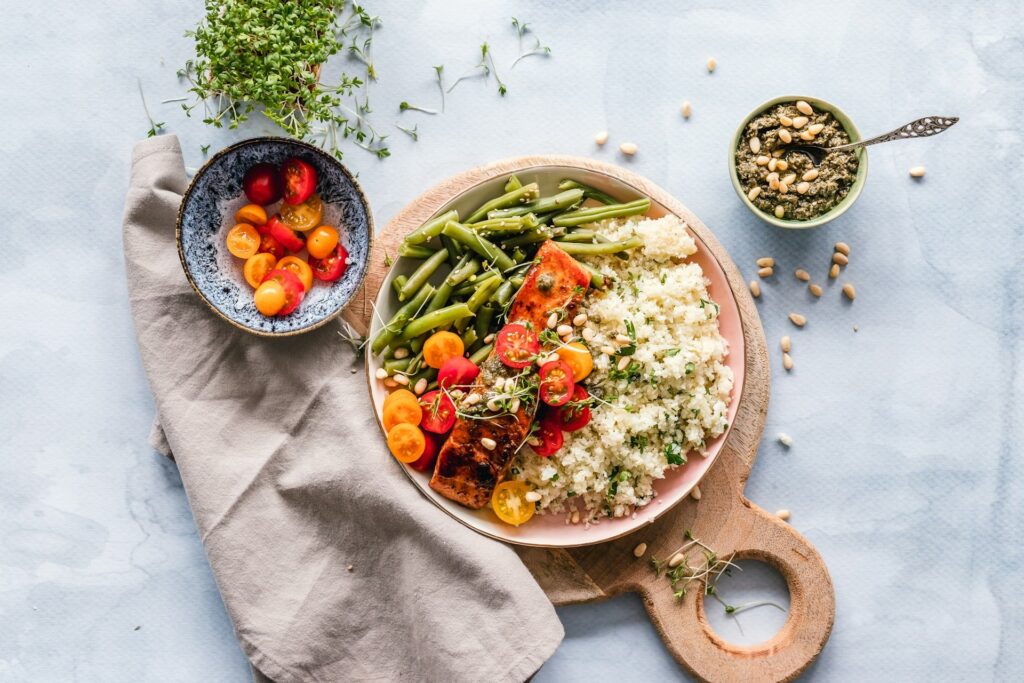 A plate of cauliflower rice topped with salmon, accompanied by green beans and cherry tomatoes.