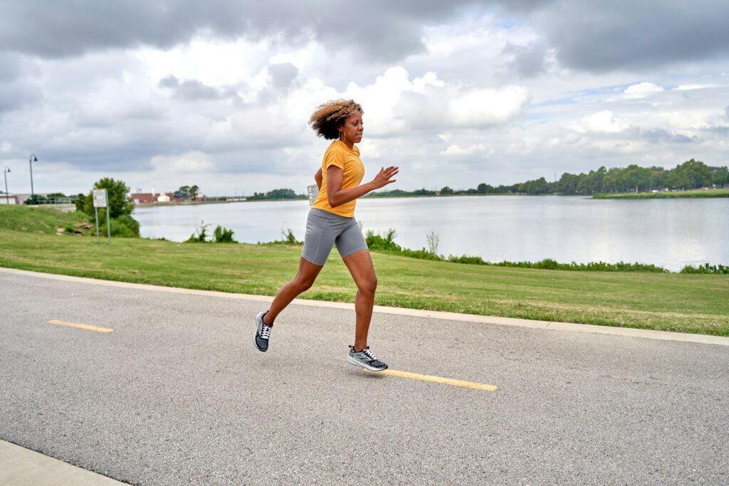 Woman with curly blonde hair running on a paved path in a park