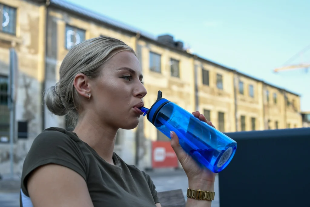 Woman sipping from a blue reusable water bottle