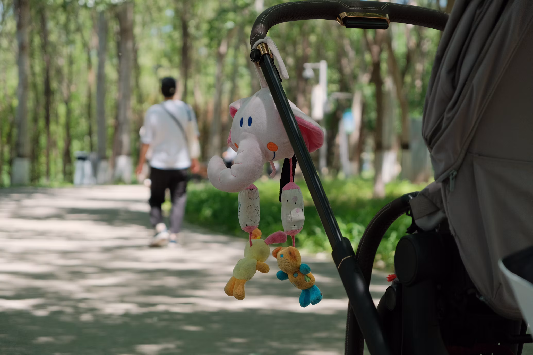 A stuffed animal handing on stroller on an outdoor trail.