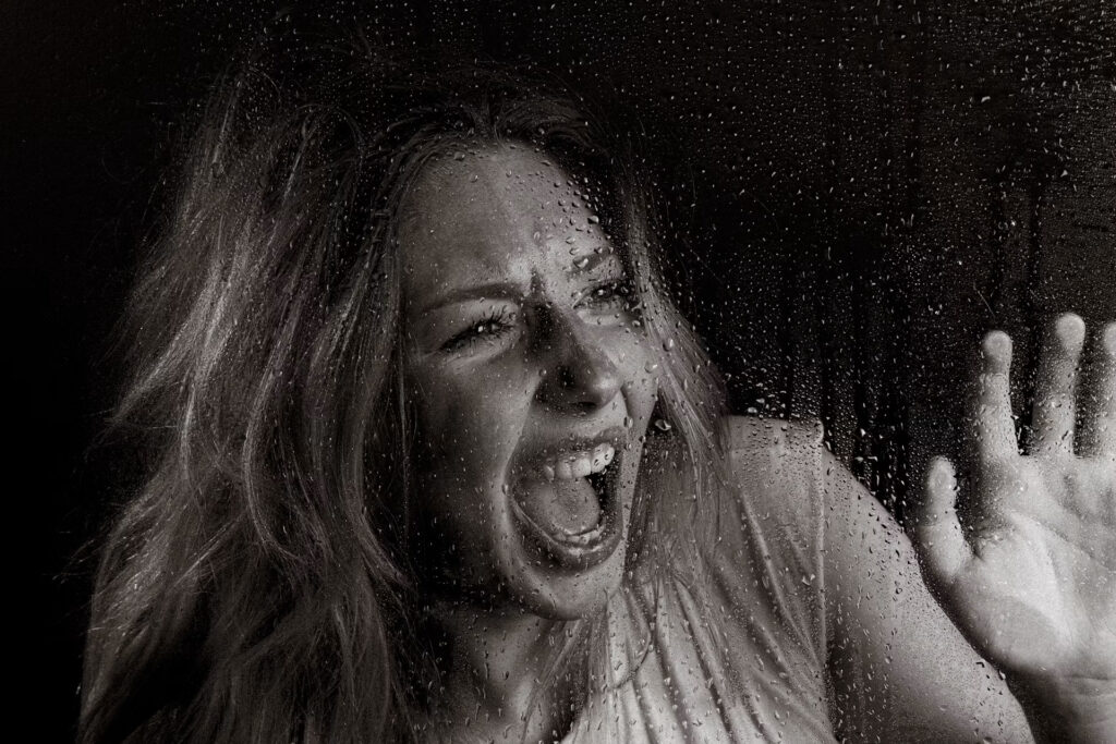 grayscale woman screaming through wet glass