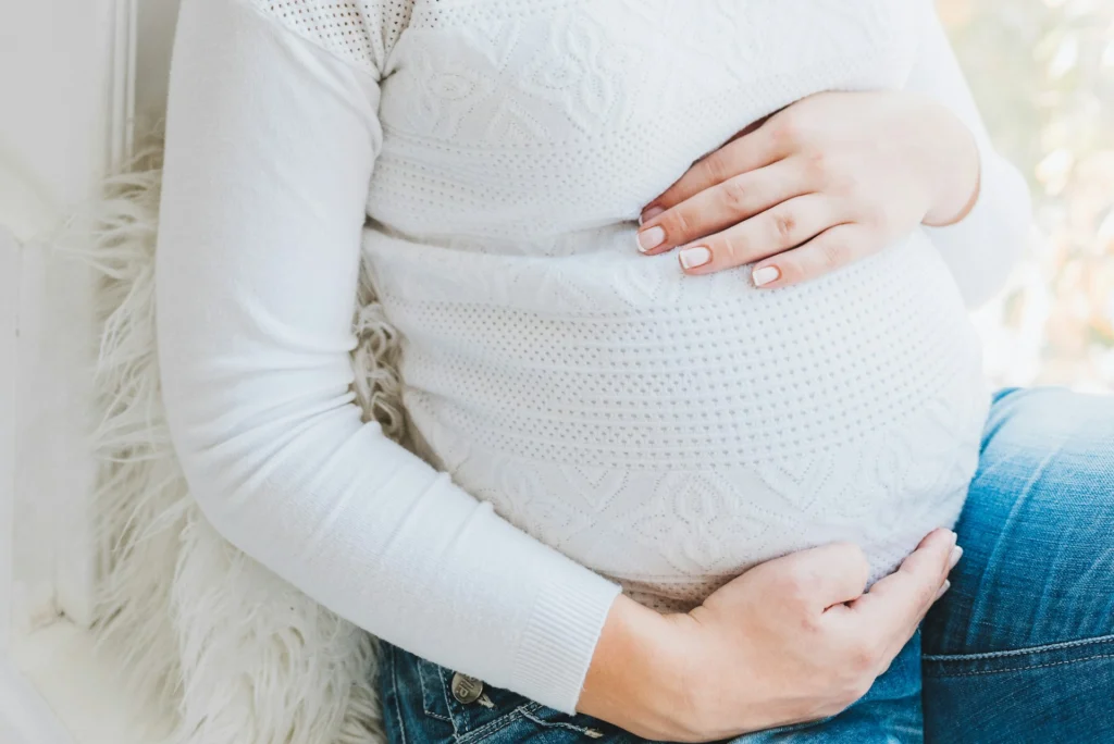 Pregnant woman in white sweater holding her belly